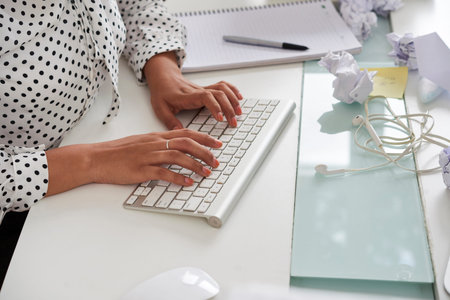 Hands of elegant female entrepreneur typing on keyboard, pieces of crumpled paper and documents in...