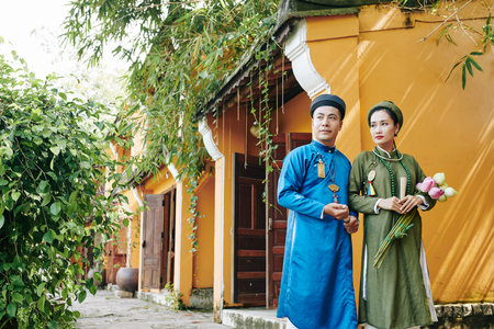 Young Vietnamese couple in traditinal costumes walking along street after wedding ceremony