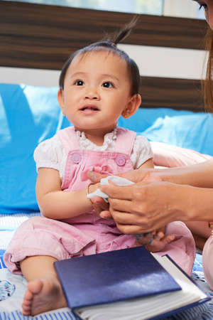 Smiling little girl sitting on bed when her mother wiping her hands trying get marker off of skinの写真素材