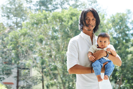 Portrait of smiling young father holding little son in his hands when stading on playground in local...