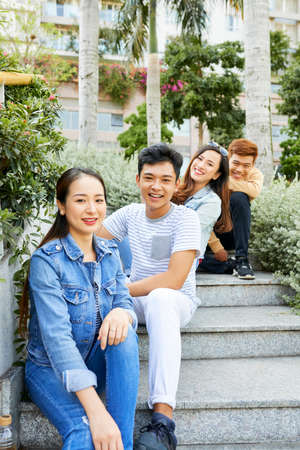 Young positive men and women sitting on steps and looking at cameraの写真素材