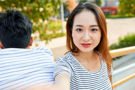 Beautiful positive young Asian woman taking selfie outdoorsの写真素材