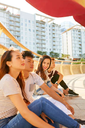 Smiling pretty young woman spending time with her best friends sitting on bridge and enjoying good weatherの写真素材