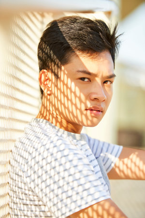 Portrait of frowning serious young man standing outdoors with shade on face and looking at camera