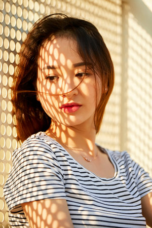 Portrait of pensive young beautiful woman with shadow net on her face standing outdoors