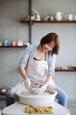 Happy pretty young smiling woman attending pottery class for beginners and making clay potの写真素材