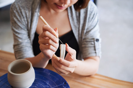 Close-up image of creative young woman carving handle of clay jar she made on potters wheel