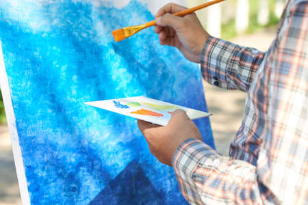 Close-uo of unrecognizable man using color palette while painting background on easel outdoorsの写真素材