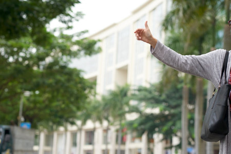Unrecognizable woman in gray cardigan standing on street and waving hand while catching taxi