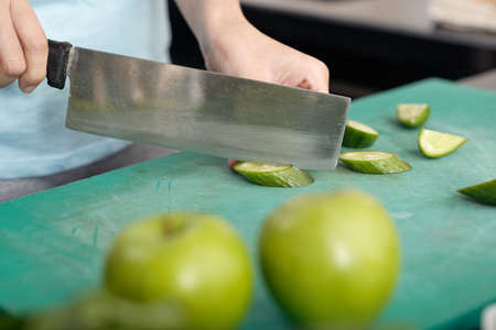 Close-up of unrecognizable woman using vegetable knife while cutting cucumber on boardの写真素材