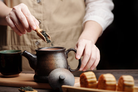 Man adding dried green tea leaves in ceramic pot when preparing drink for mid autumn festivalの写真素材