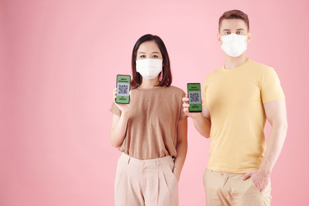 Diverse couple showing smartphones with covid-19 vaccine passports and QR codes on screen