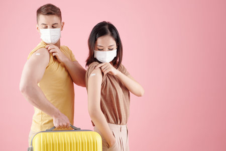Young couple in medical masks showing shoulders with plaster aid after coronavirus Covid-19 vaccine