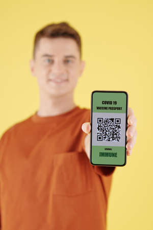 Smartphone with covid-19 vaccine passport in hand of smiling young manの写真素材