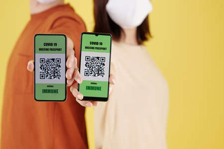Close-up image of couple showing smartphones with QR codes after getting vaccine against coronavirusの写真素材