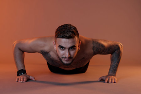 Shirtless determined fit muscular young man doing push-ups and looking at camera