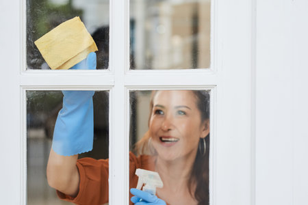 Smiling mature woman cleaning dirty windows in her apartment