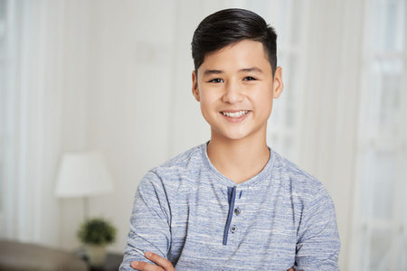 Portrait of positive teenge boy standing in living room and smiling at camera