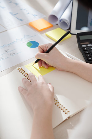 Hands of entrepreneur writing on yellow sticky note after working with charts and reportsの写真素材