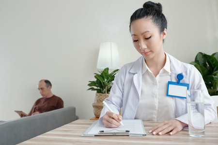 Young female general practitioner filling medical card when senior patient with tablet computer...