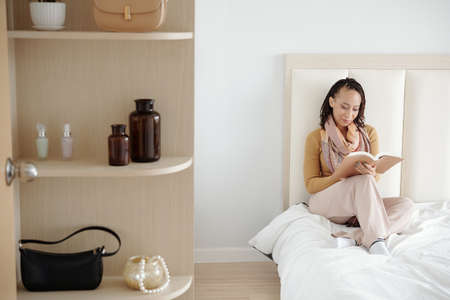 Smiling woman reading novel at home when staying in her apartment due to lockdownの写真素材