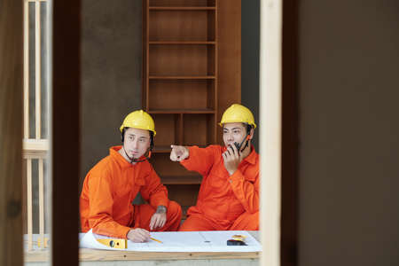 Young Asian foreman talking on walkie-talkie when explaining contractor where to unload building materialsの写真素材