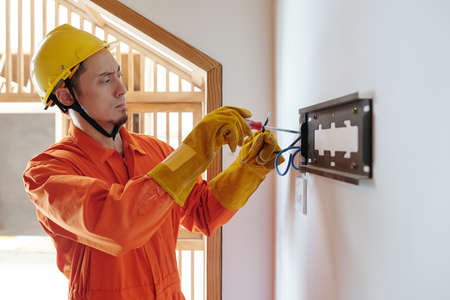 Serious frowning electrician in protective gloves installing electricity meter in houseの写真素材