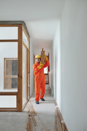Young Vietnamese worker walking along house corridor and carrying heavy wooden building materials