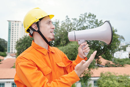 Portrait of construction site worker with loudspeaker standing on rooftop and supervising...