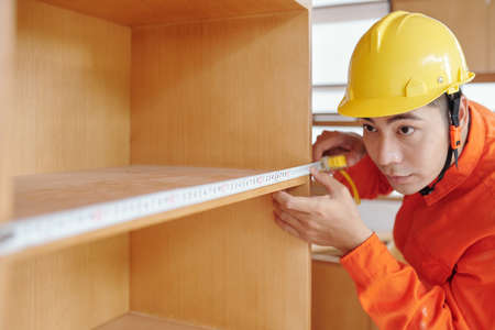 Workman using tape measure when measuring and installing shelvesの写真素材