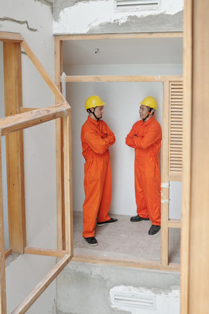 Positive contractors standing inside building under construction and discussing rennovation process