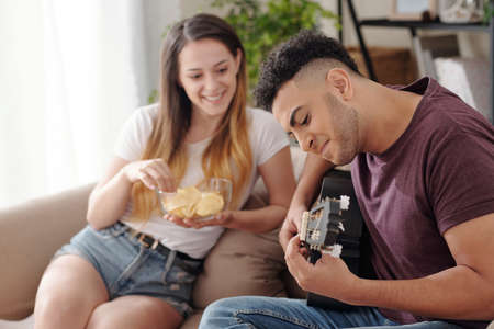Joyful young woman looking her talented boyfriend showing how good he is playing guitar after a few lessons he tookの写真素材