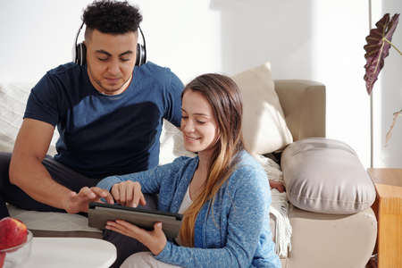 Smiling cheerful young couple ordering food delivery online via application on tablet computerの写真素材