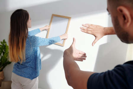 Man explaining girlfriend how to turn the picture frame to hang on the wall it evenlyの写真素材