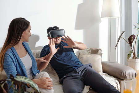 Man in virtual reality headset playing scary video game when staying home with girlfriend due to lockdownの写真素材