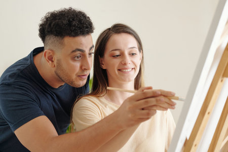 Creative young man painting on canvas with hand of his girlfriendの写真素材