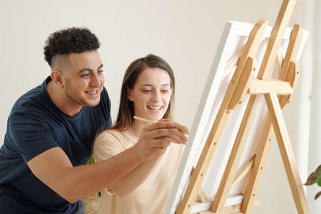 Positive young couple enjoying painting picture on canvas when staying home due to lockdownの写真素材