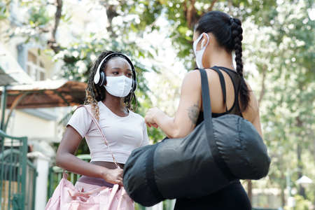 Pretty fit young women in protective masks standing outdoors and discussing trainingの写真素材