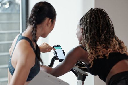 Fitness trainer checking heart rate of female client via application on smartphone