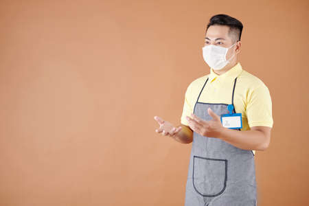 Portrait of waiter or barista in medical mask actively gesturing when talking, isolated on brownの写真素材