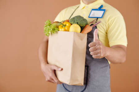 Grocery store worker holding package of food and showing thumbs-upの写真素材