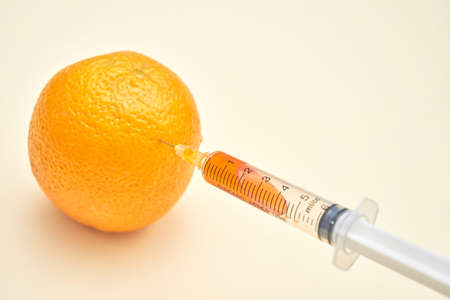 Close-up of syringe injecting orange with orange liquid, gmo conceptの写真素材