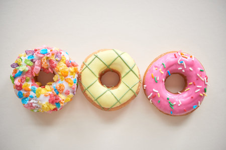 Directly above view of three multi-colored doughnuts with frosting and sprinkles against isolated...