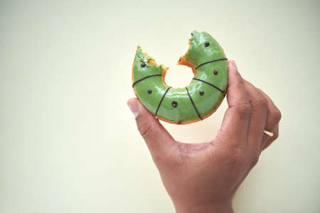 Close-up of hand holding bitten glazed donut against isolated backgroundの写真素材