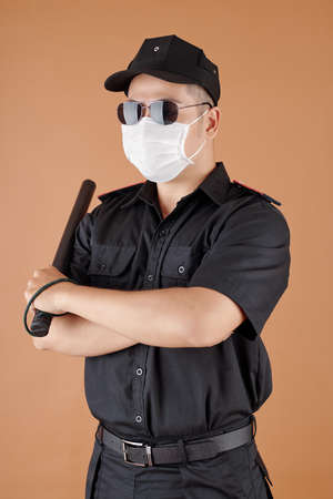 Confident police officer in sunglasses and protective mask standing with baton in handsの写真素材