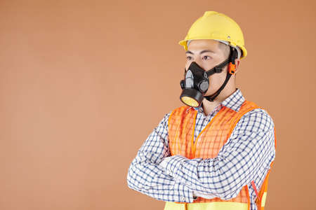 Construction worker wearing hardhat and respirator when standing in studio with arms foldedの写真素材