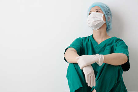 Tired nurse in scrubs and protective mask sitting on the floor in clinic corridor and resting after hard dayの写真素材