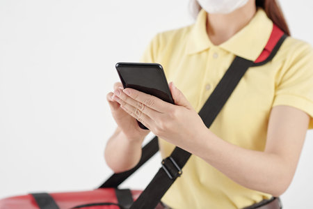 Young female courier receiving order of customer via application on smartphone