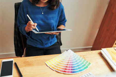 Unrecognizable female cartoon designer sitting at wooden table with color swatch and using digitizerの写真素材