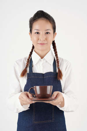 Portrait of positive young waitress serving cup of tasty coffee to customer in coffeeshopの写真素材